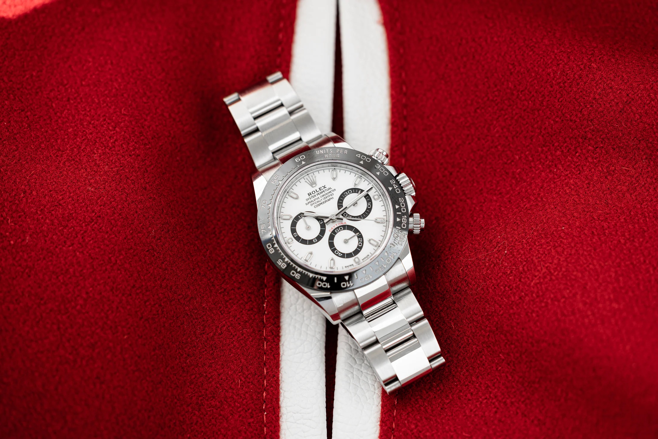A Rolex Daytona watch with a white dial rests on top of a red and white fabric