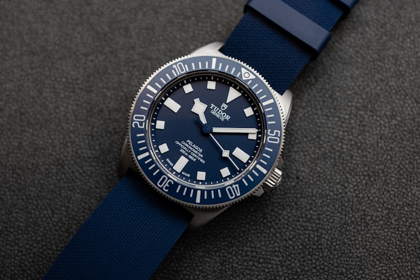 The Pelagos FXD laying on a table with a blue rubber strap. 
