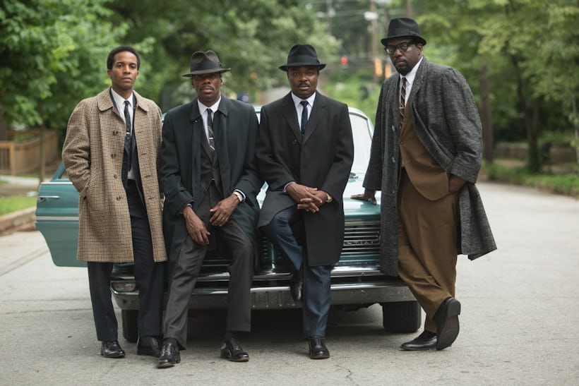 King (Oyelowo), with overcoat, Stetson, and Datejust and three other lean on a 1960s car on a neighborhood street in Selma.