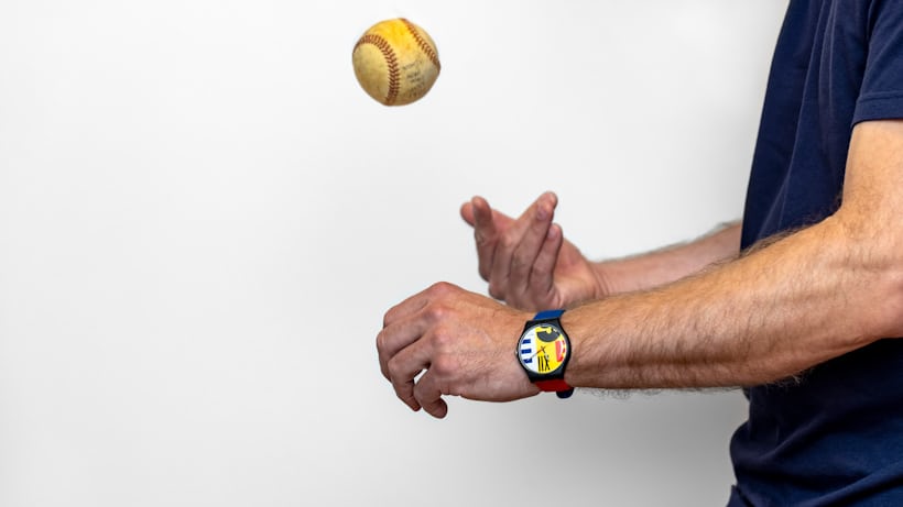 A person throwing a baseball and wearing a Swatch watch 