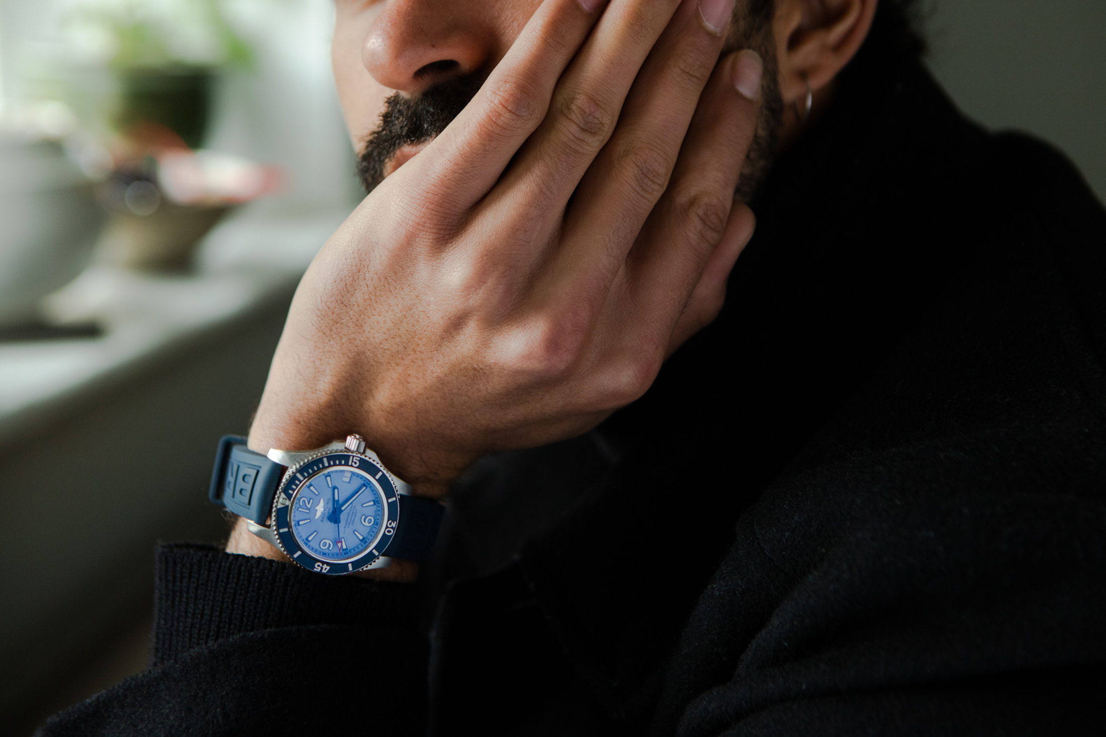 A blue Breitling watch on the wrist of a person resting their head in their hands