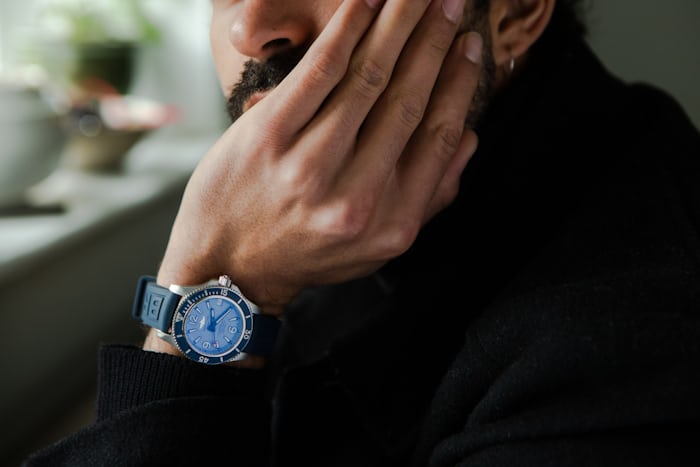A blue Breitling watch on the wrist of a person resting their head in their hands