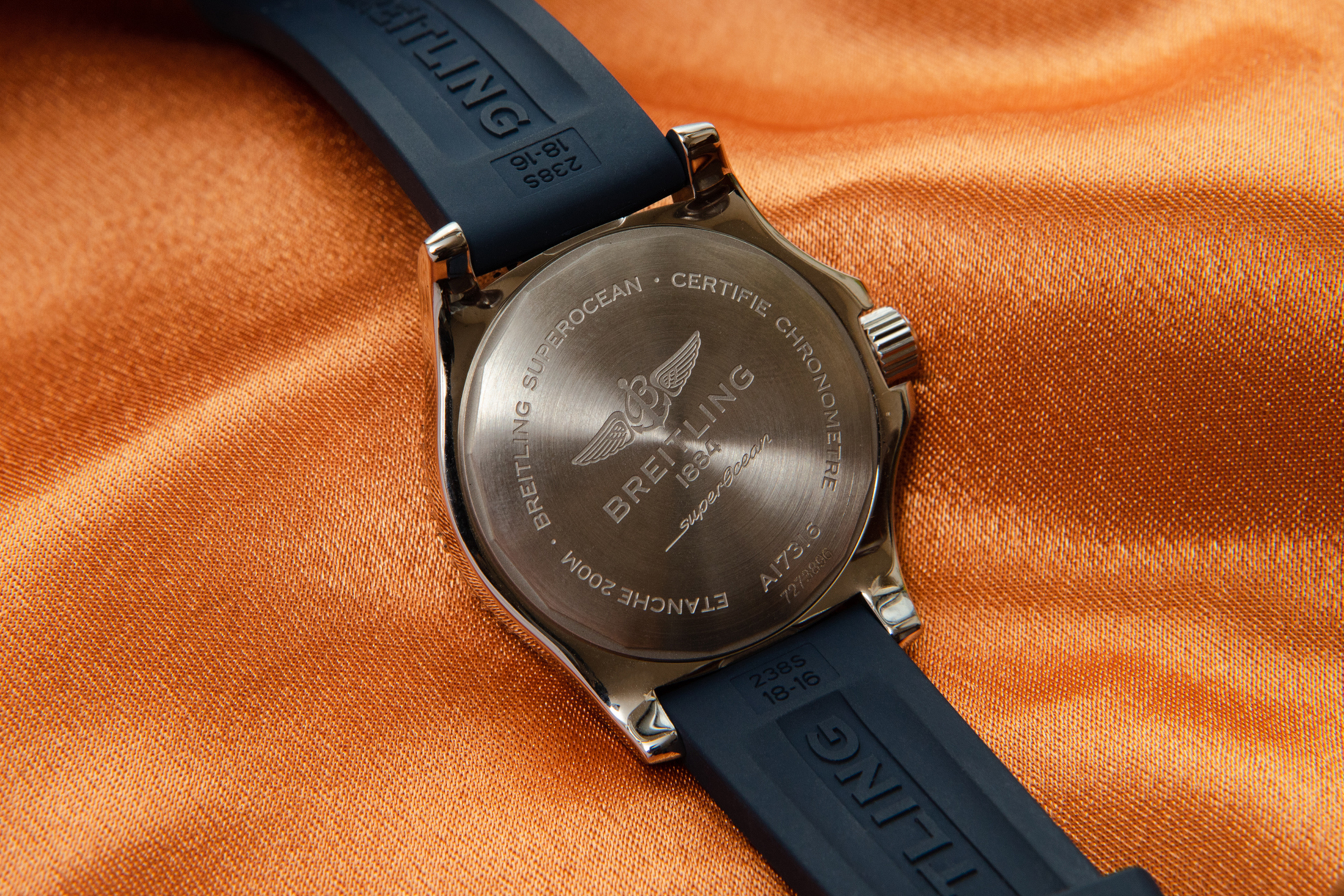 The caseback of a watch on an orange fabric background