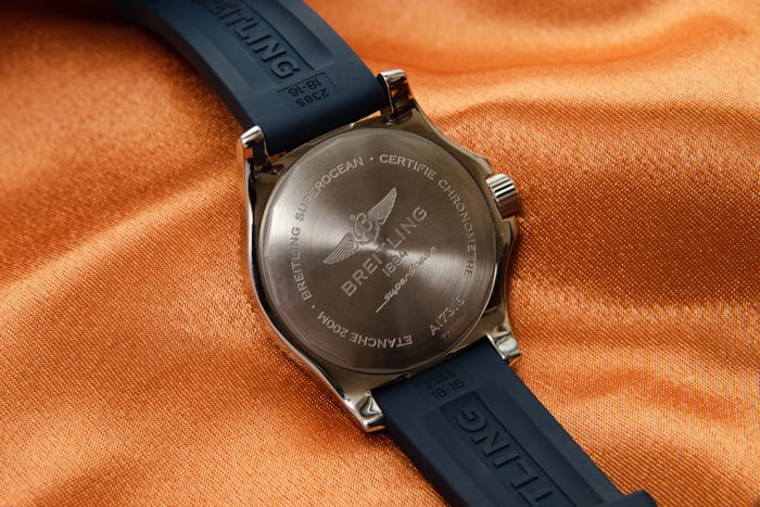 The caseback of a watch on an orange fabric background