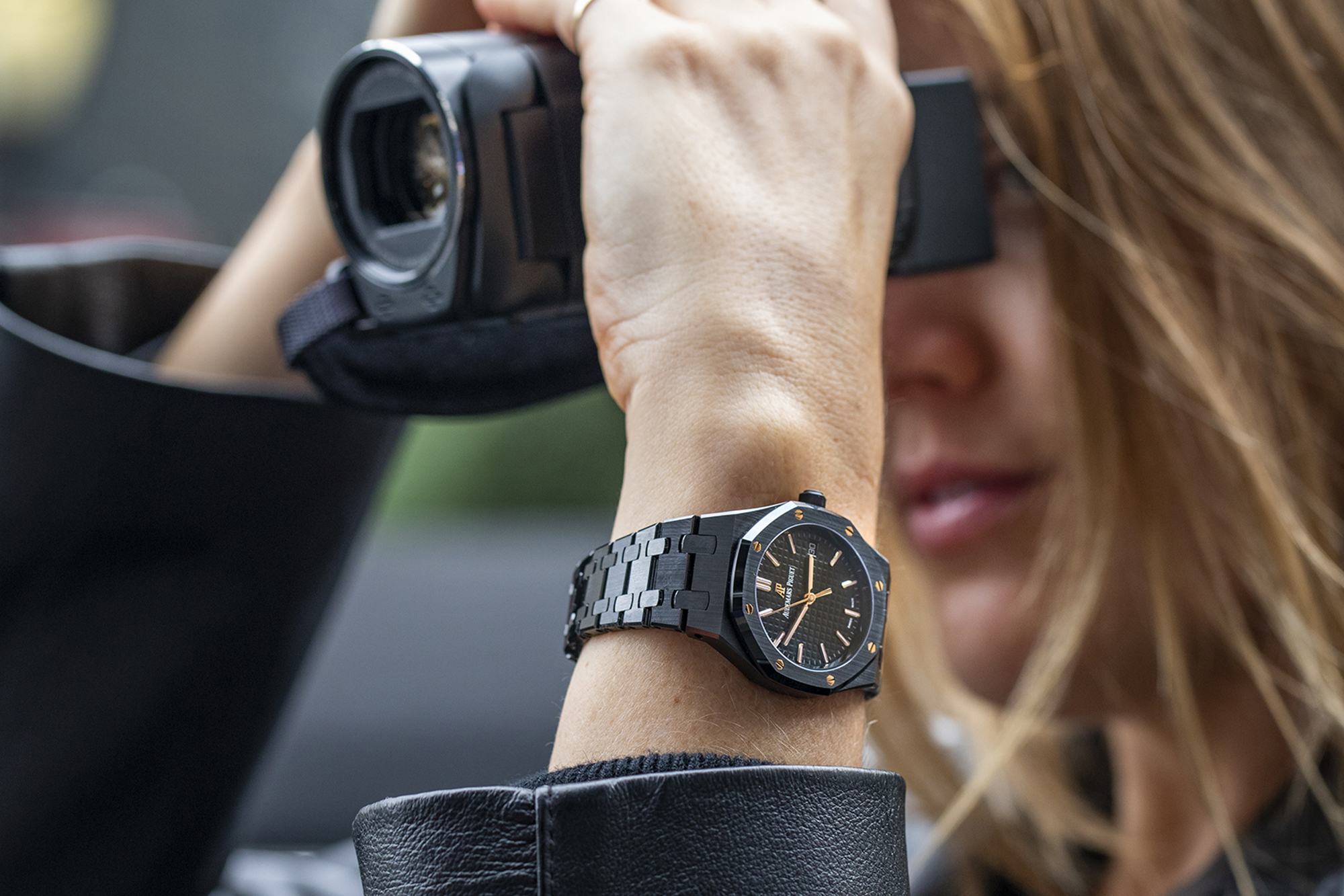 A person holding a video recorder with a Royal Oak on their wrist