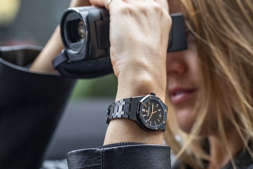 A person holding a video recorder with a Royal Oak on their wrist