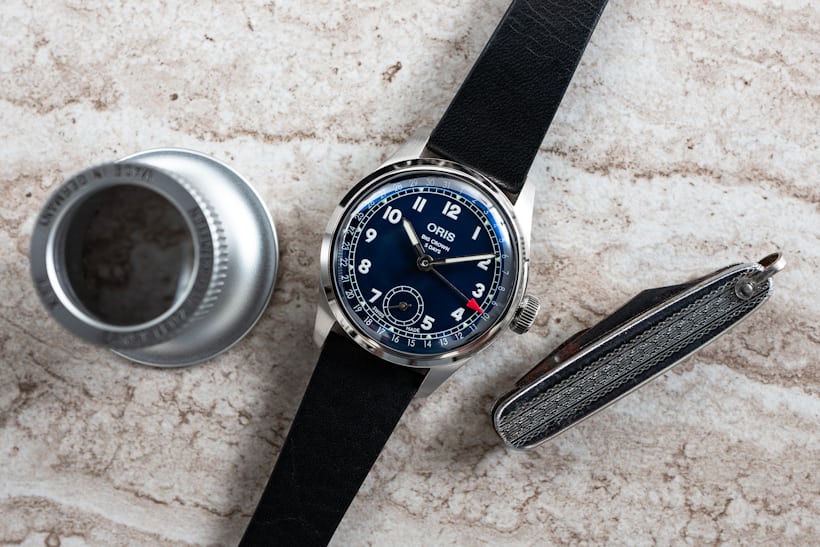 An Oris BC 403 on a table with a loupe and a small folding knife. 