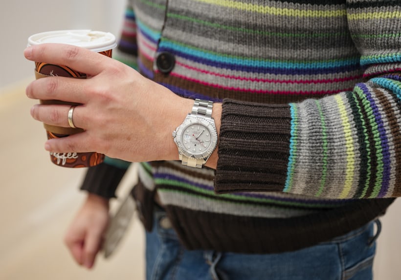 A man wears a Rolex Yachtmaster and holds a cup of coffee.