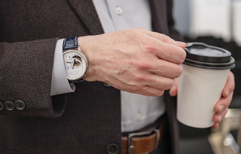 A man in a brown blazer wears an A. Lange & Söhne Richard Lange Tourbillon 'Pour le Mérite' and holds a cup of coffee