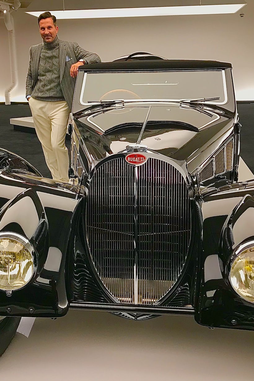 A man poses next to a vintage car