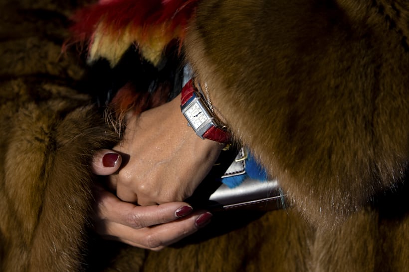 The hands of a person wearing a fur coat and a watch on a red strap