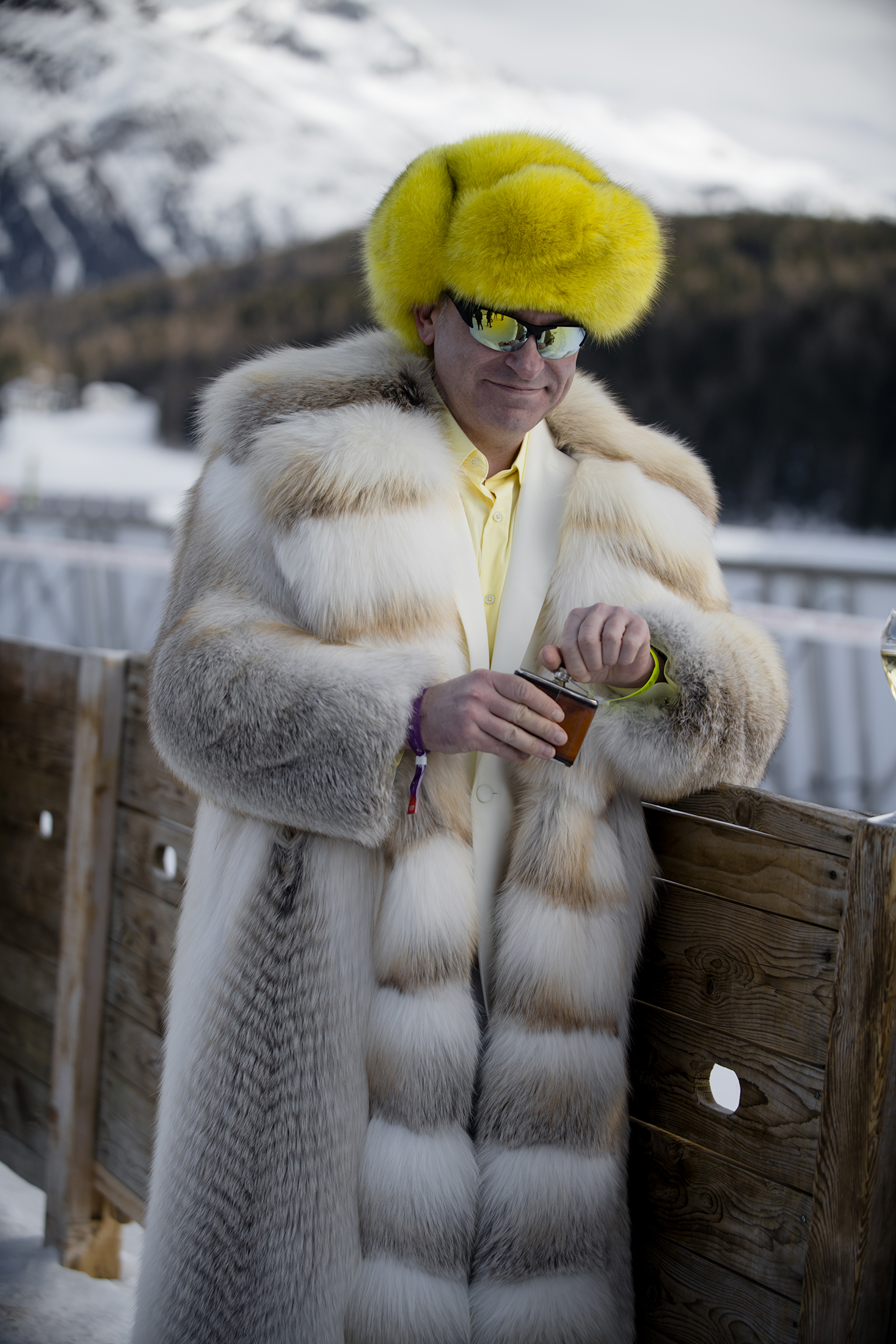 A person in a white fur coat leaning against a fence