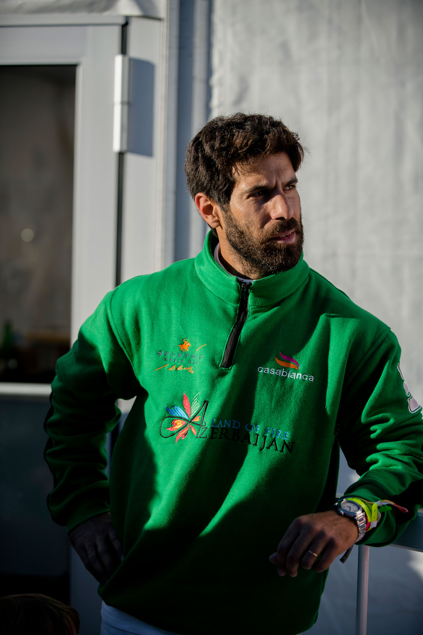 A man in a green jacket leans against a fence 