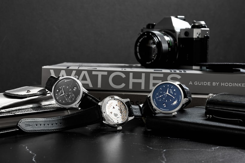 A group shot of three Glashütte Original Pano watches; books and a camera are visible in the background. 