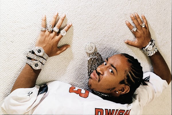 Rapper, Ludacris, laying on a white carpet wearing multiple watches.