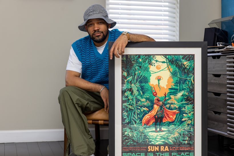 A man in a bucket hat posing next to a bright green poster