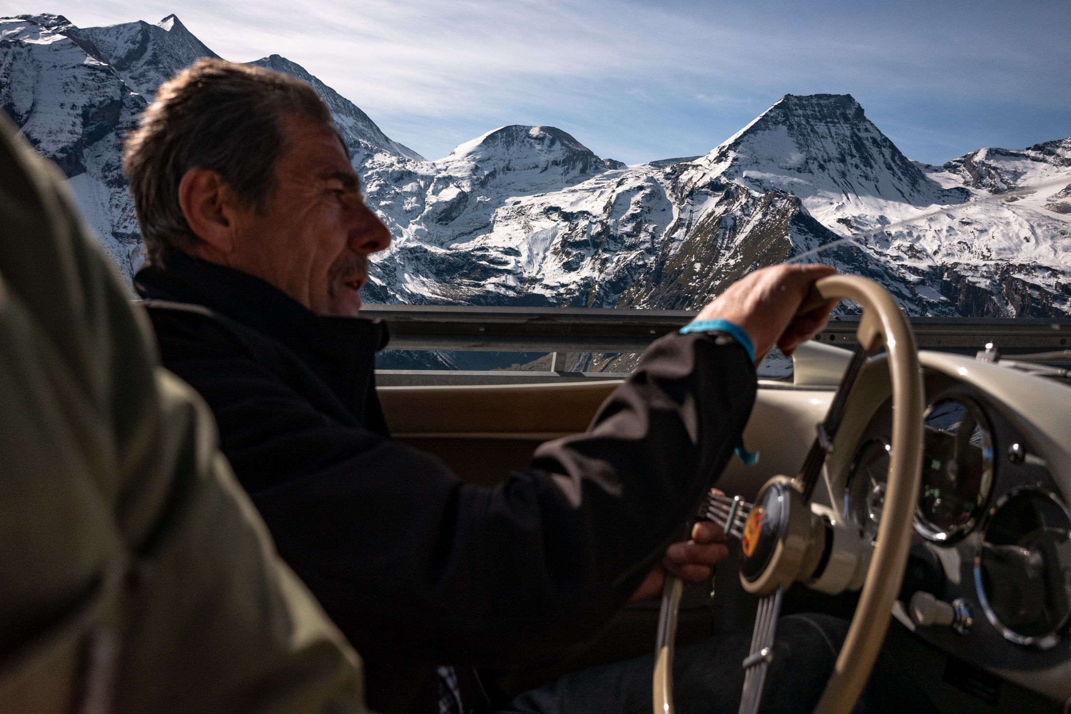 a man driving a porsche 550 on a road. 
