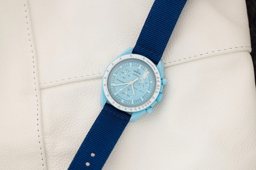 A Moonswatch Uranus on a blue Nato strap rests on top of a white textured surface