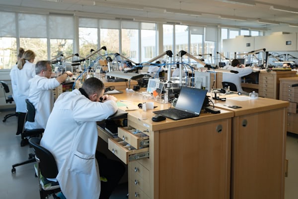 Interior wide shot of a watchmaking studio with various watchmakers sitting at desks in an open floor plan office building