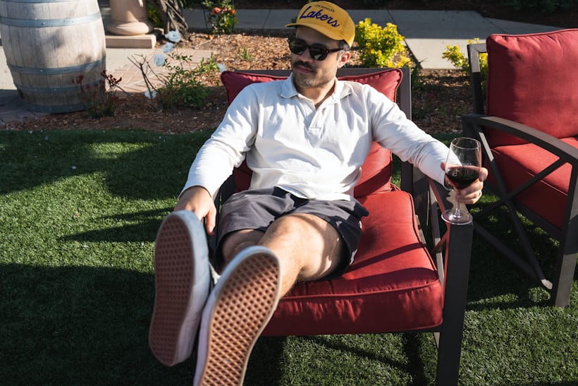 Hodinkee Editor Brandon Menancio sits with his feet propped up in a lounge chair outdoors while holding a glass of red wine