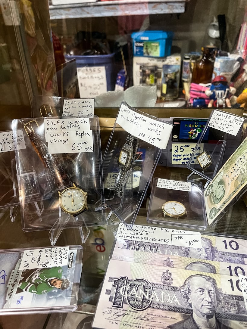 A cabinet with several vintage watches, hockey cards, and currency. 