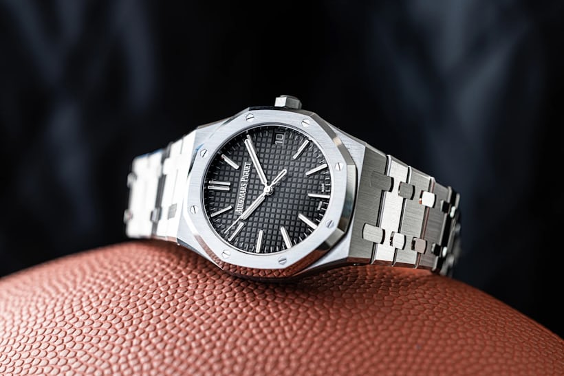 An AP Royal Oak watch with a gray dial rests on its side on top of a textured surface