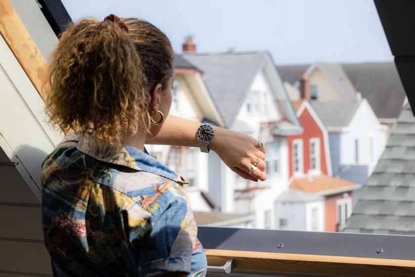 チューダー　ブラックベイ 54の腕時計を腕につけながら、高層住宅の窓から外を眺める女性