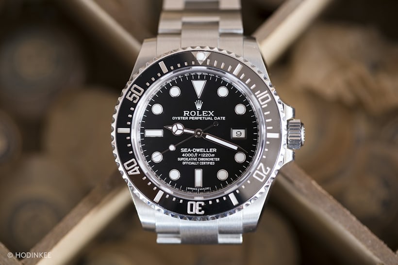 A Rolex Sea-Dweller 116600 sits face-up with a wooden background.
