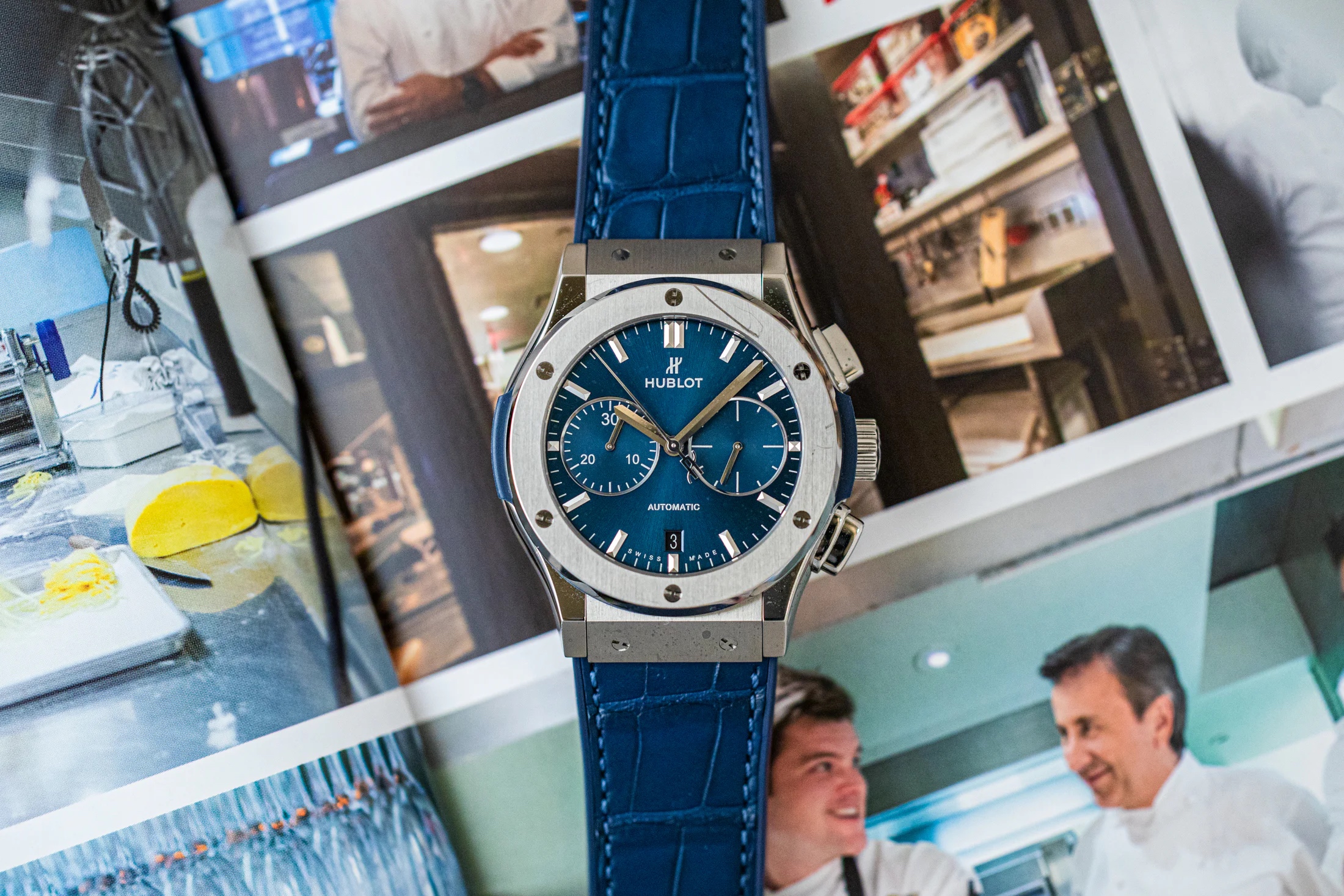 Hublot with a blue dial on top of a book featuring photos of Daniel Boulud and his restaurant