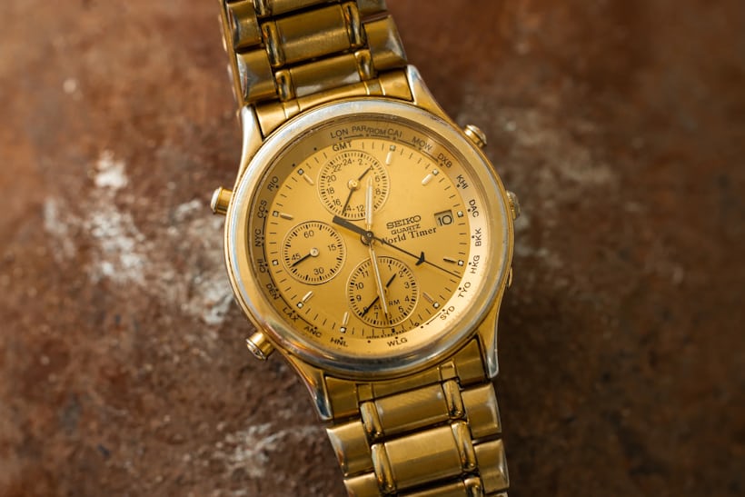 A gold Seiko World Timer watch on top of a brown concrete background
