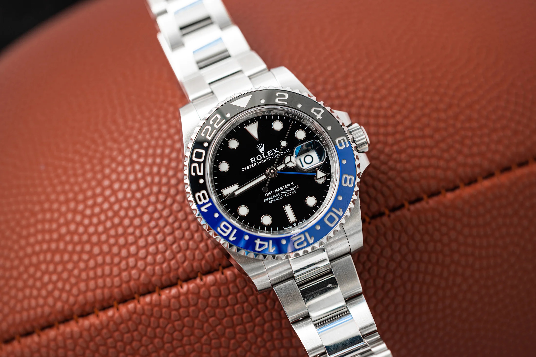 A Rolex GMT Batman watch rests on top of a football