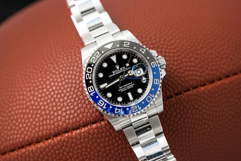 A Rolex GMT Batman watch rests on top of a football