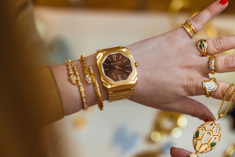 A woman wearing multiple gold rings models the bulgari octo finissimo watch on her wrist