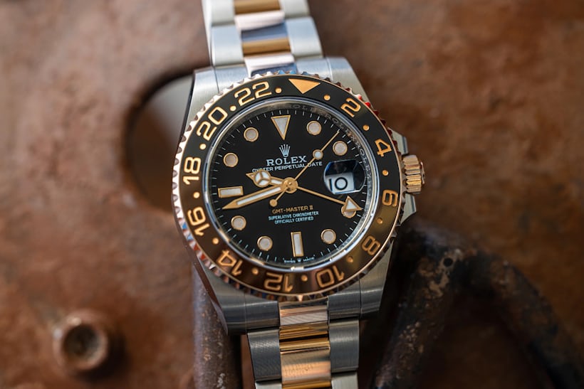 A Rolex GMT Root Beer watch rests on top of a rusty surface