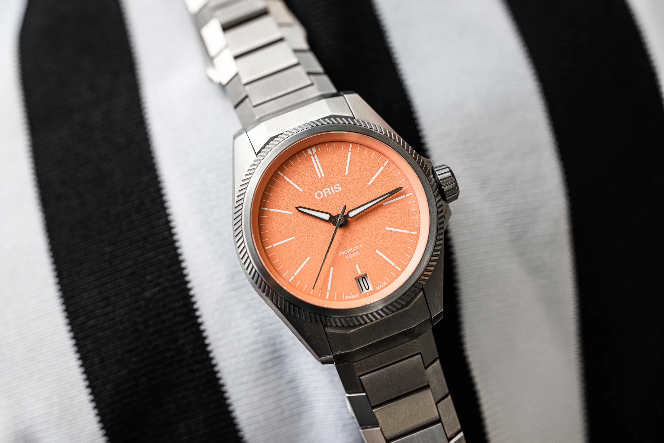 An Oris ProPilot X Calibre 400 watch with a salmon dial rests on top of black and white fabric