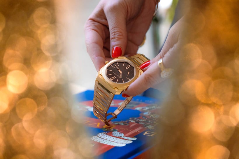 Woman with painted red nails handles the bulgari octo finissimo watch between two blurred foreground objects