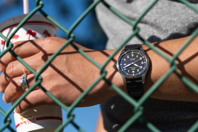 watch on wrist while holding cup behind a green fence