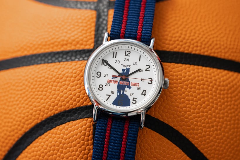 A Timex watch with a custom logo on the dial featuring a silhouette of a man riding a horse with the words "BOSTON WATCH SHOTS" in red rests on top of a basketball
