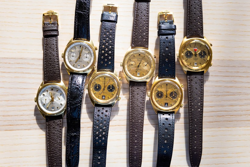 A group of carreras with c-shaped cases with gold dials and gold finishings laid out on a wooden surface