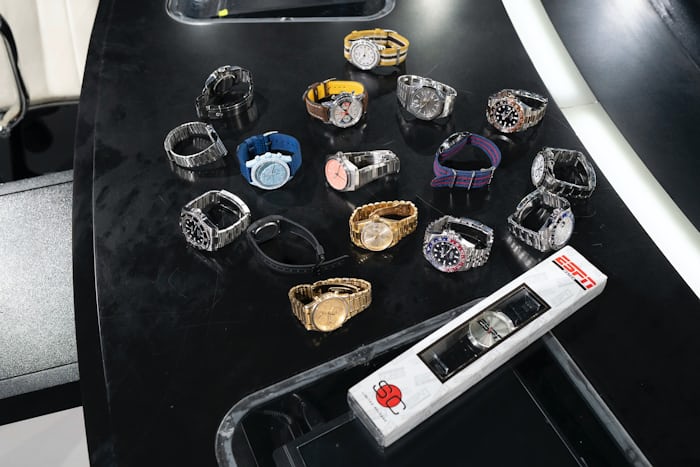 A collection of brand-name watches of varying sizes and colors is laid out on a curved black desk