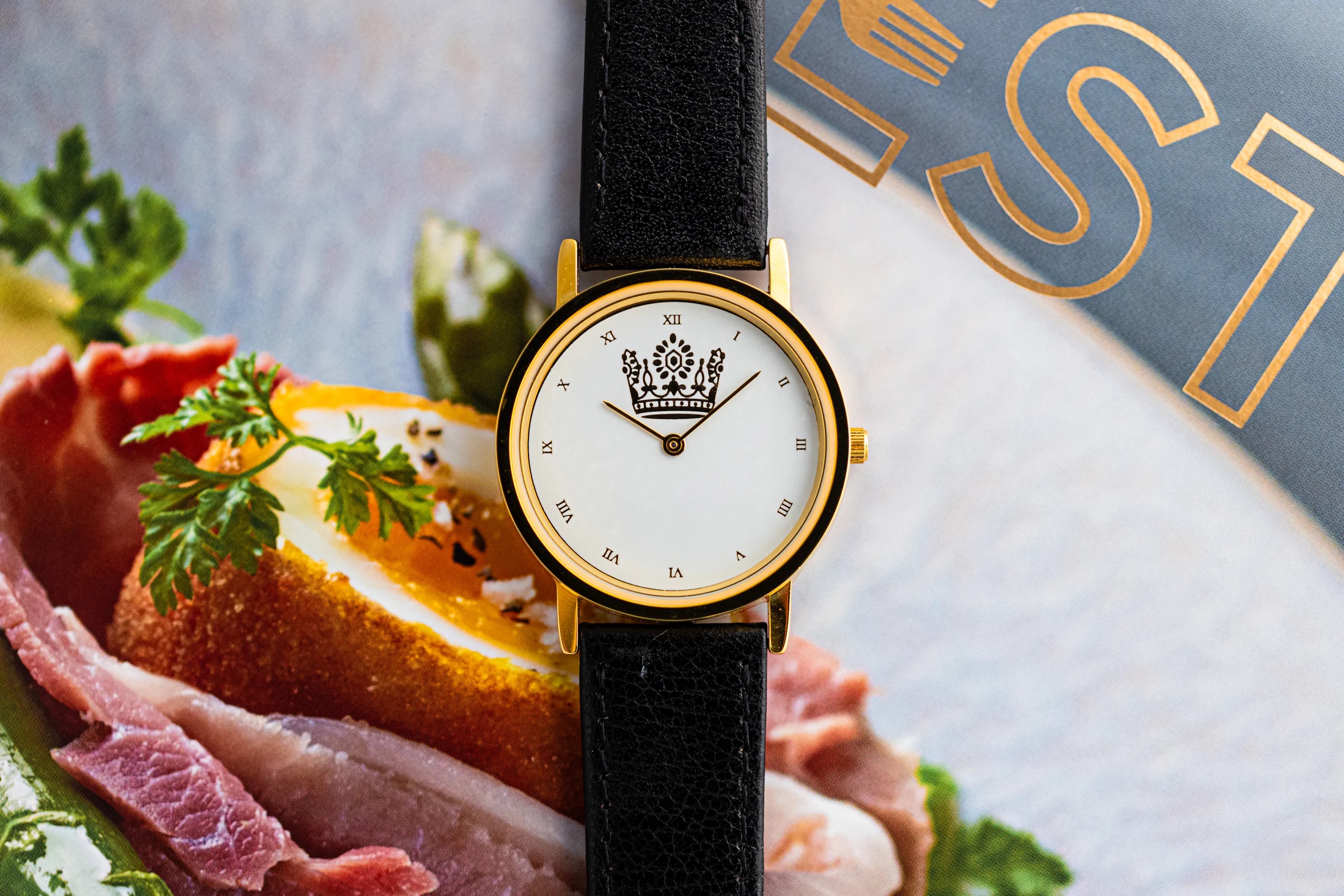 Crown Watch on top of book page featuring photo of colorful food