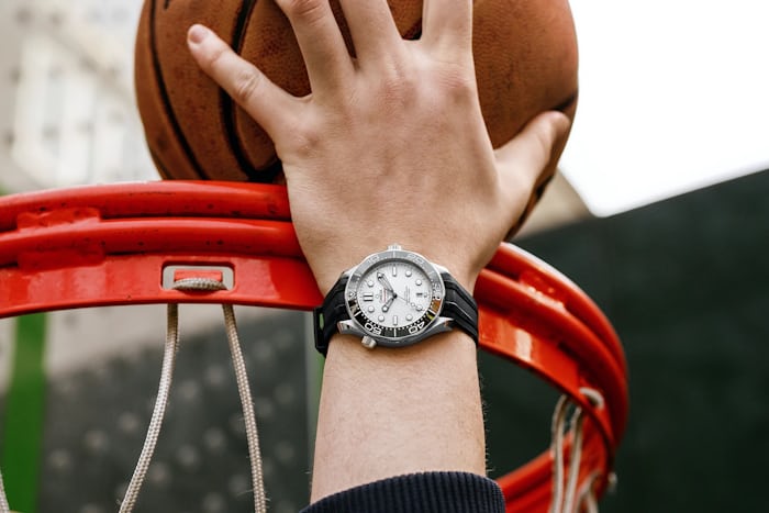 A man wears an Omega Seamaster Diver 300M while dunking a basketball.