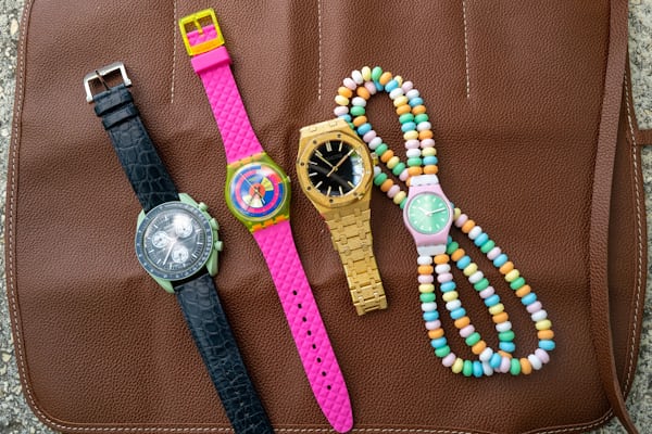 Left to right: Moonswatch, Swatch, Audemars Piguet, and another Swatch with a beaded bracelet. All of the watches are laid out side by side on a brown leather surface