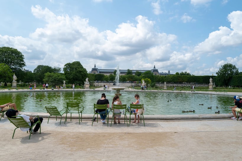 Wide shot of people sitting in chairs around a large outdoor park fountain