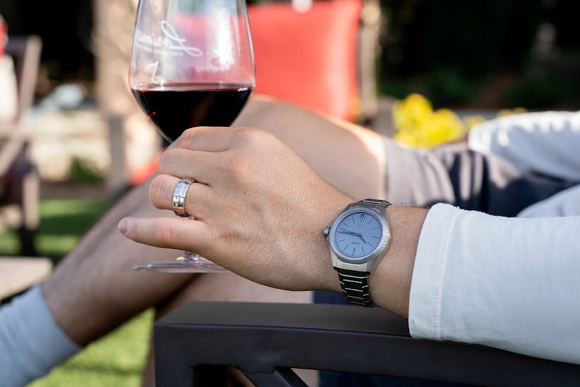 A man holds a glass of red wine while wearing the grey Oris ProPilot X Calibre 400 on his wrist