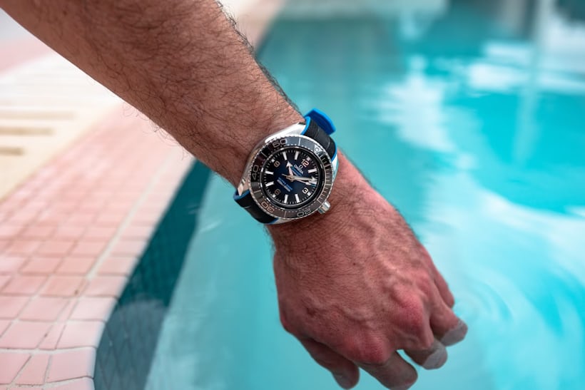 The blue dial ultra deep on a mans wrist next to a pool. 