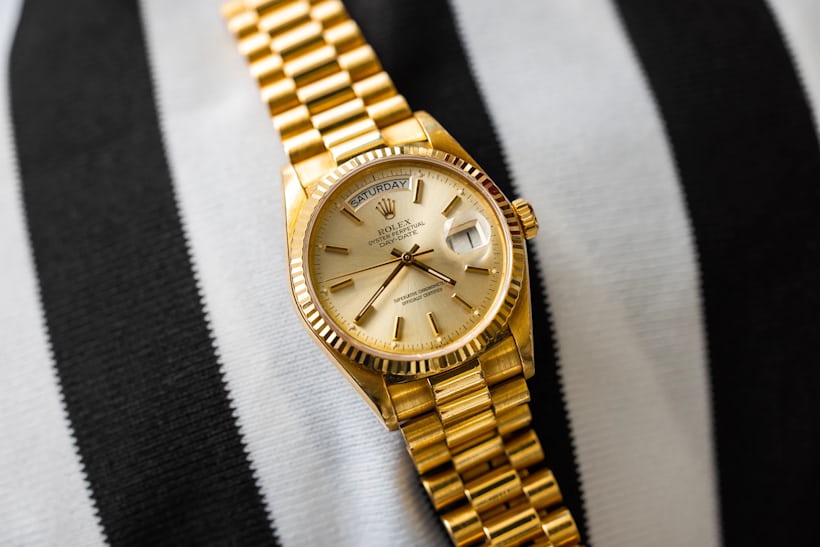 A gold Rolex Day-Date rests on black-and-white striped fabric